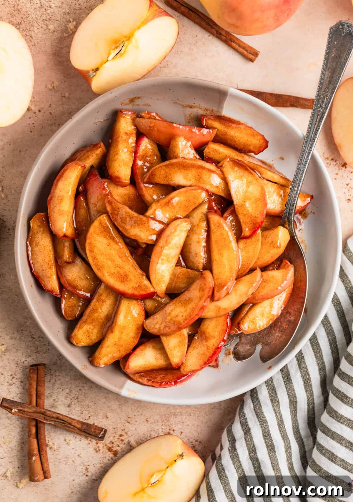 Air Fryer Cinnamon Apple Slices 9 A beautifully presented serving plate filled with buttery cinnamon fried apples, accompanied by a serving spoon and decorative cinnamon sticks.