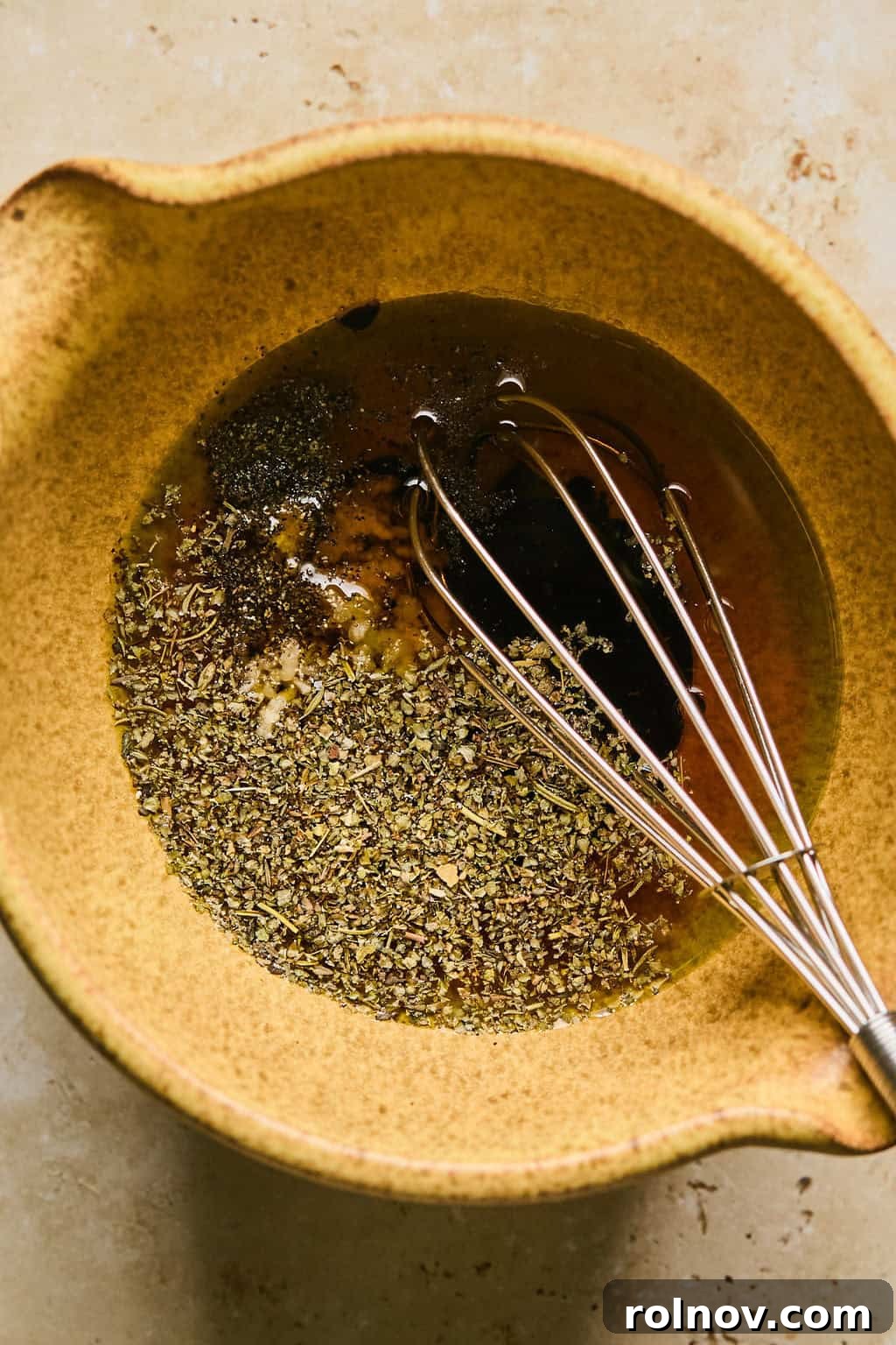 A whisk in a bowl of vibrant red sun-dried tomato dressing, ready to be poured over the pasta salad.