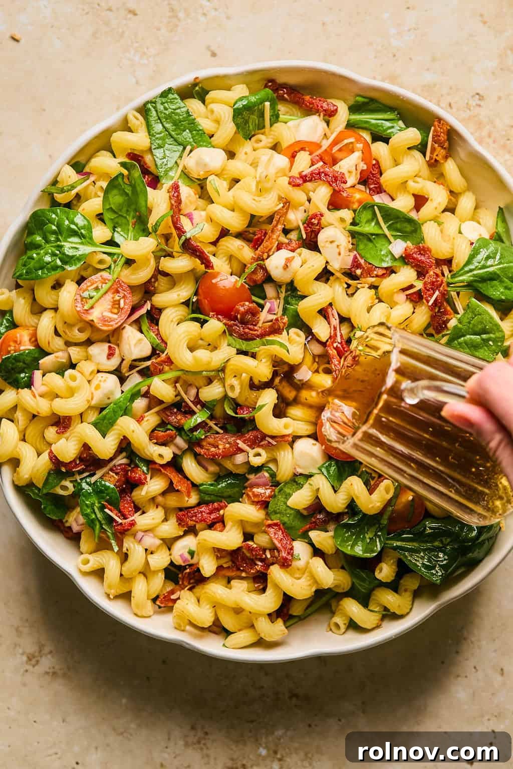 A delicious sun-dried tomato pasta salad being drizzled with its vibrant red dressing.