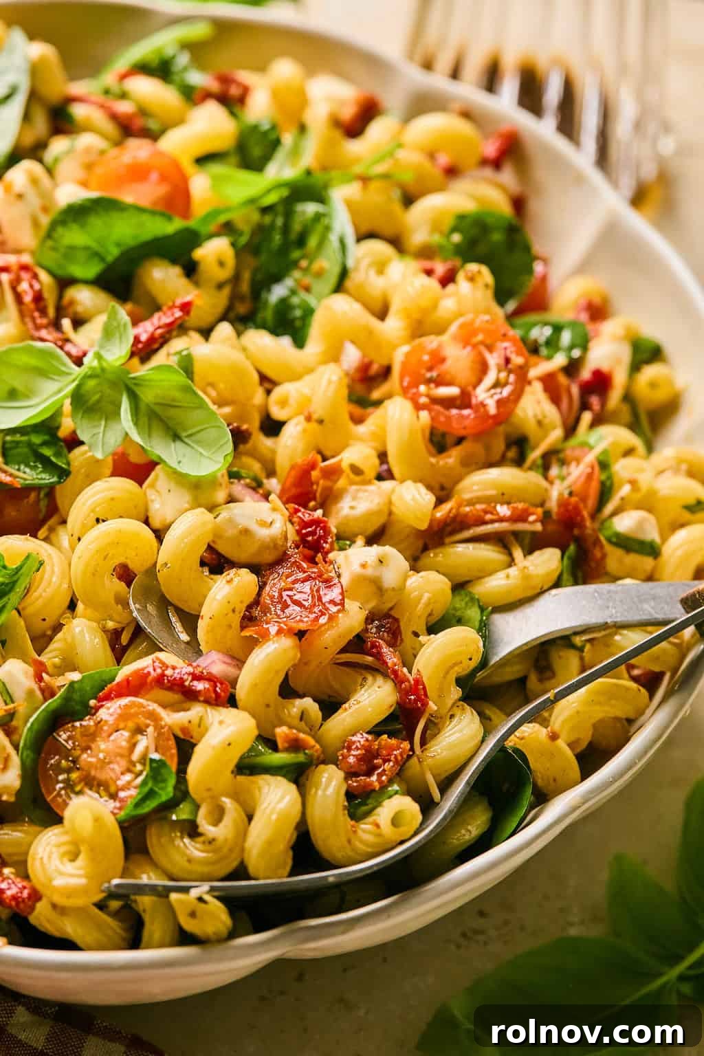 A close-up of sun-dried tomato pasta salad in a white serving dish, garnished generously with freshly chopped basil, highlighting the rich colors and textures.