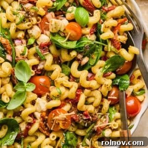 Pasta salad with sun dried tomatoes, spinach, basil and other ingredients in serving bowl.