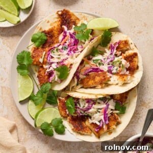 Air fryer fish tacos topped with cilantro lime slaw on plate with lime wedges. Lightly fried fish with crisp edges.