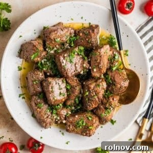 White plate with perfectly cooked air fryer steak bites in lemon garlic butter sauce, garnished with fresh parsley.