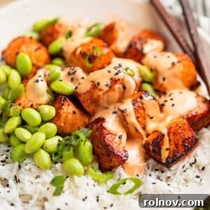 Air fryer salmon bites served with a creamy bang bang sauce on top, presented over a bed of fluffy white rice.