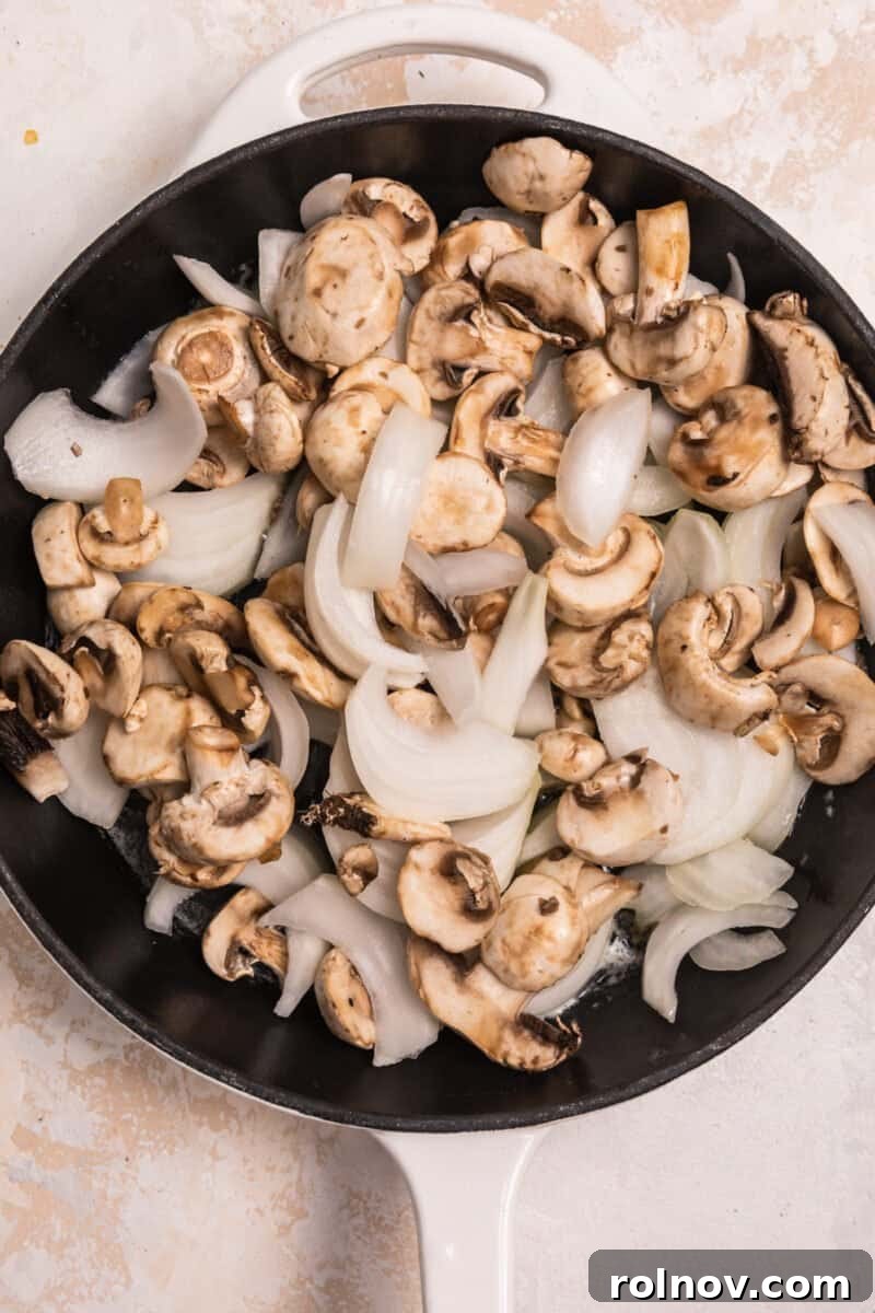 Ultimate French Dip Sliders 3 Overhead view of cast iron skillet with raw onion and mushrooms in butter, beginning to soften.