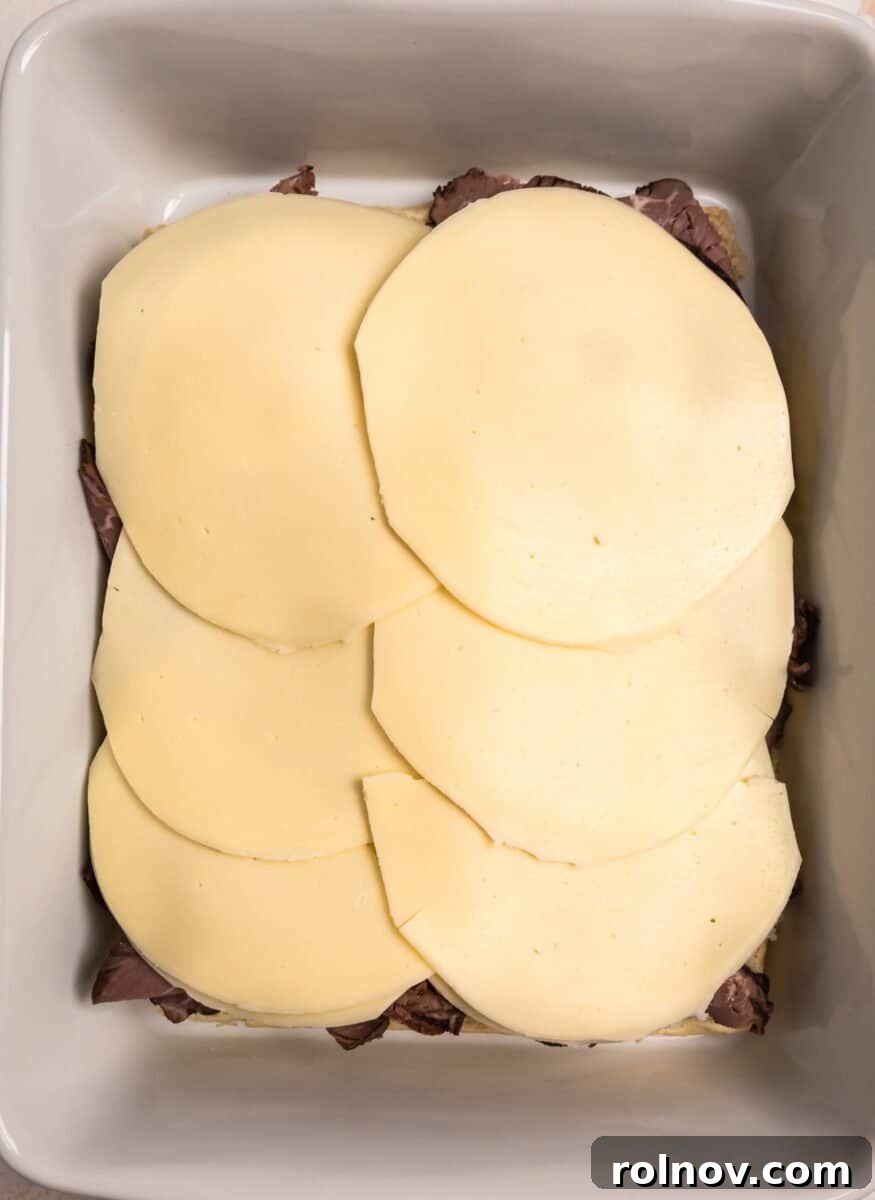 Ultimate French Dip Sliders 7 Provolone cheese slices covering the roast beef layer in the baking dish.