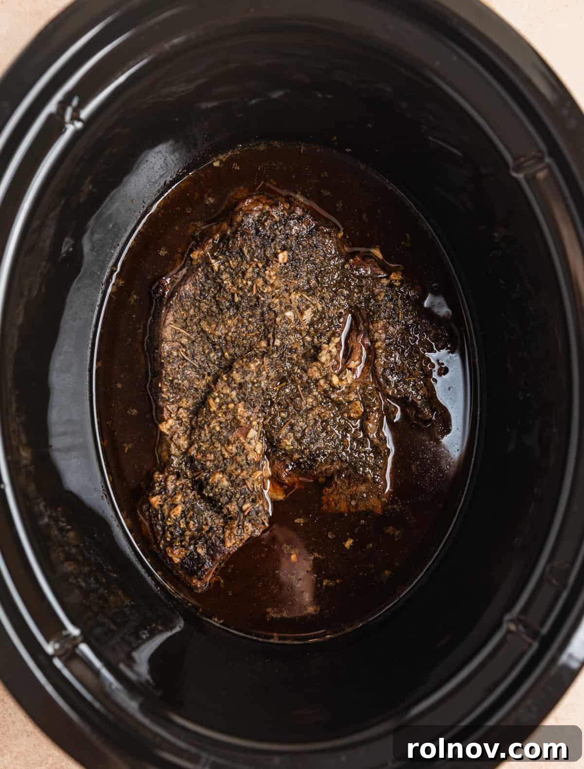 Overhead view of cooked chuck roast in juices in slow cooker.