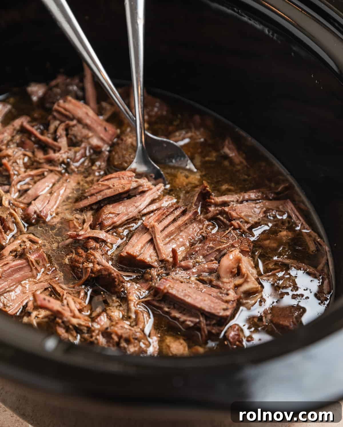 Forks shredding crock pot shredded beef in slow cooker.
