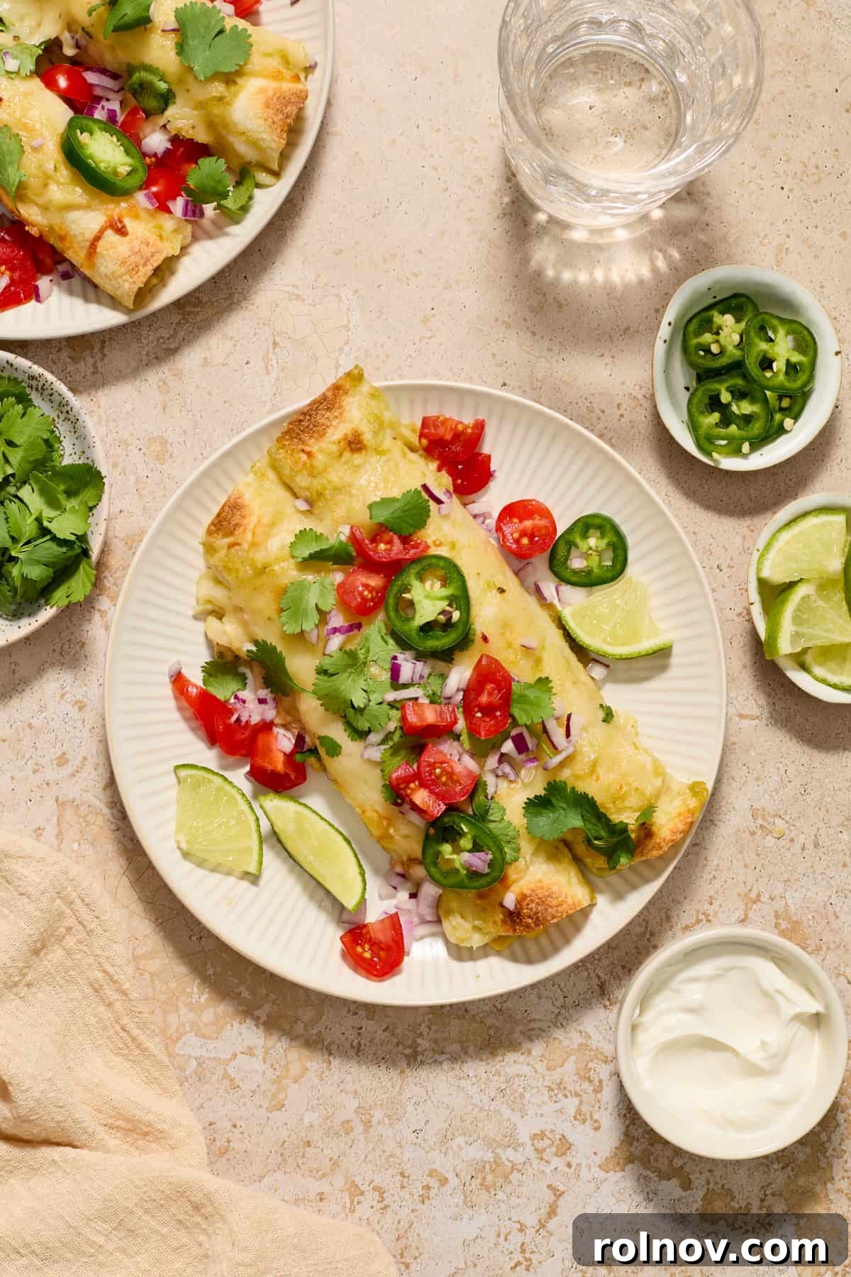 Zesty Verde Chicken Enchiladas 12 Chicken enchiladas on white plate topped cilantro, tomatoes and jalapeños.