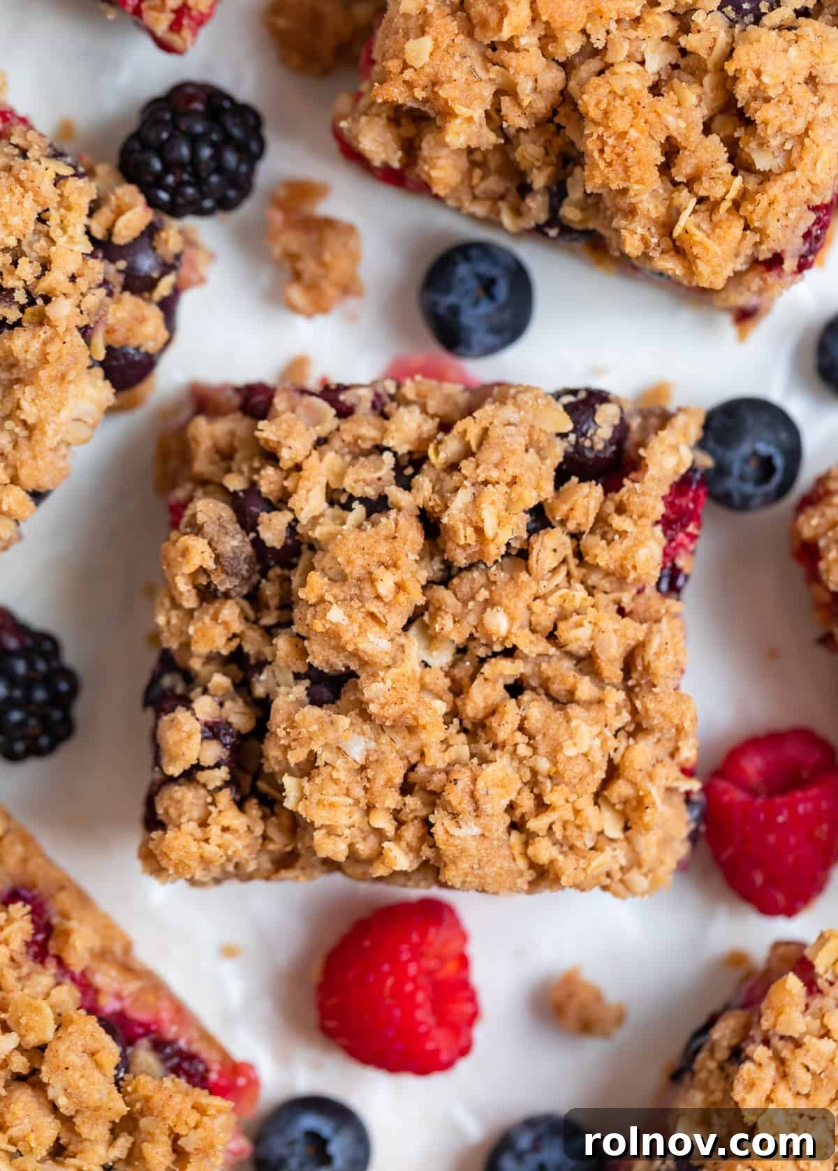 Golden Berry Crumble Bars 8 Mixed berry oat bars with crumble topping on white background with fresh berries and crumbles surrounding.