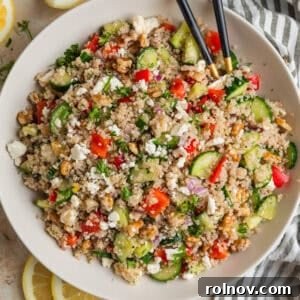 Cucumber quinoa salad in bowl with peppers, feta, chopped dill and serving utensils.