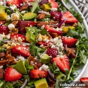 Strawberry arugula goat cheese salad on white serving plate topped with balsamic dressing.