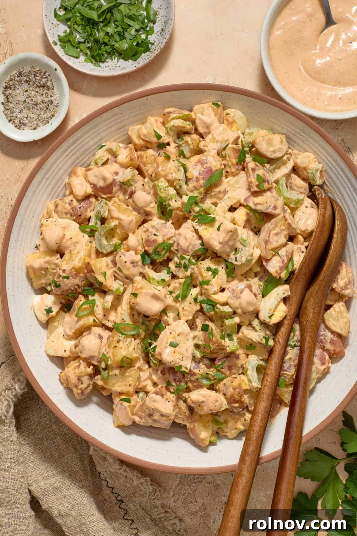 Bayou Potato Salad 2 Cajun potato salad in dish with serving utensils propped in bowl, garnished with fresh herbs.