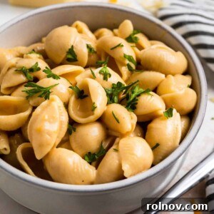 Creamy macaroni and cheese shells in clay bowl with chopped fresh parsley on top.