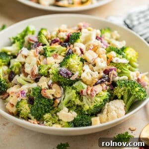 Broccoli cauliflower salad in bowl tossed with cheese, cranberries, bacon and more.