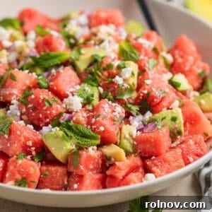 Bowl with watermelon salad with feta and avocado and spoon scooping into it.