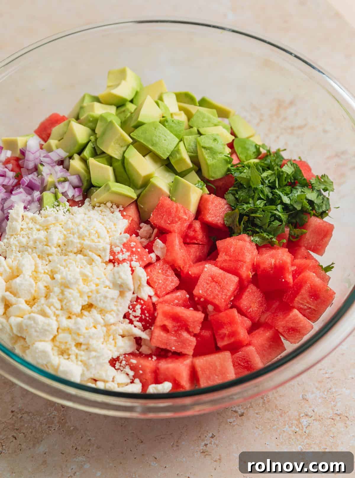Watermelon Avocado Feta Harmony 5 A large glass bowl filled with diced avocado, crumbled feta cheese, chopped cilantro, red onion, and watermelon cubes, before mixing.