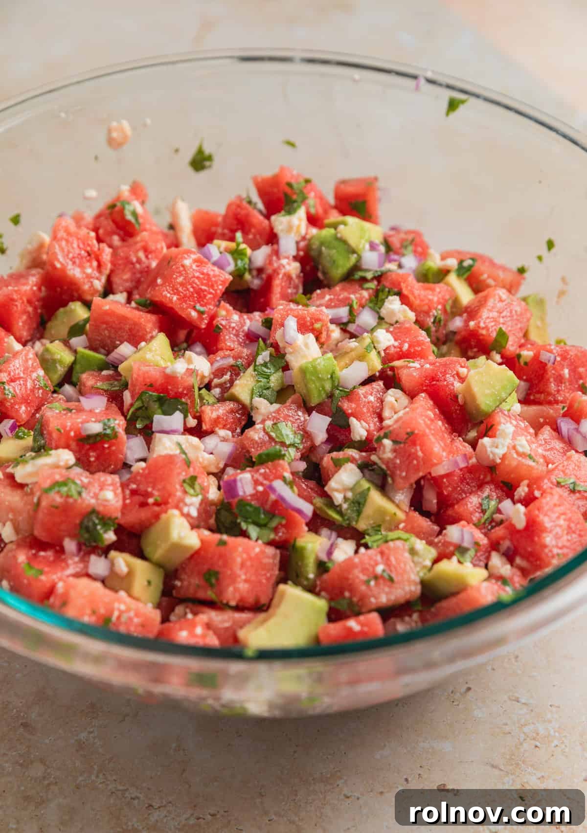 Watermelon Avocado Feta Harmony 7 The watermelon avocado feta salad gently tossed in a large glass bowl, coated with dressing.