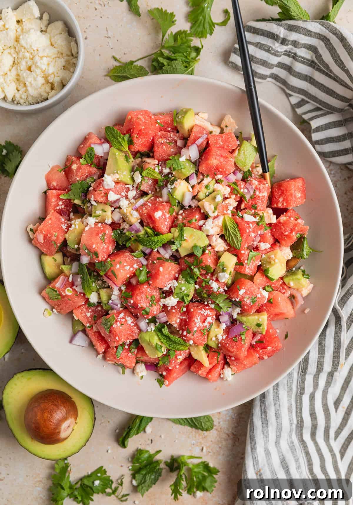 Watermelon Avocado Feta Harmony 8 Overhead view of a vibrant watermelon and feta salad in a bowl, with a spoon and artfully sliced avocado beside it.