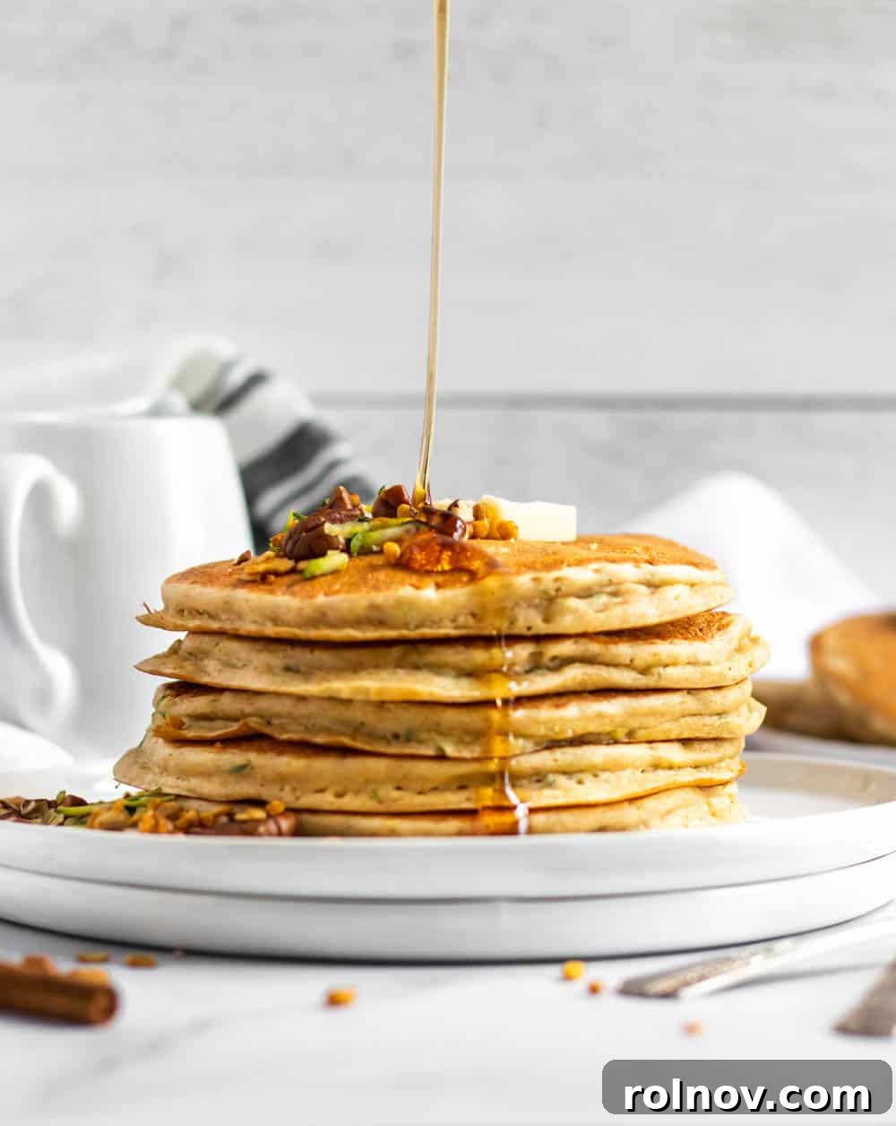 Wholesome Zucchini Oat Pancakes 2 Zucchini oat flour pancakes on a plate, drizzled with maple syrup.