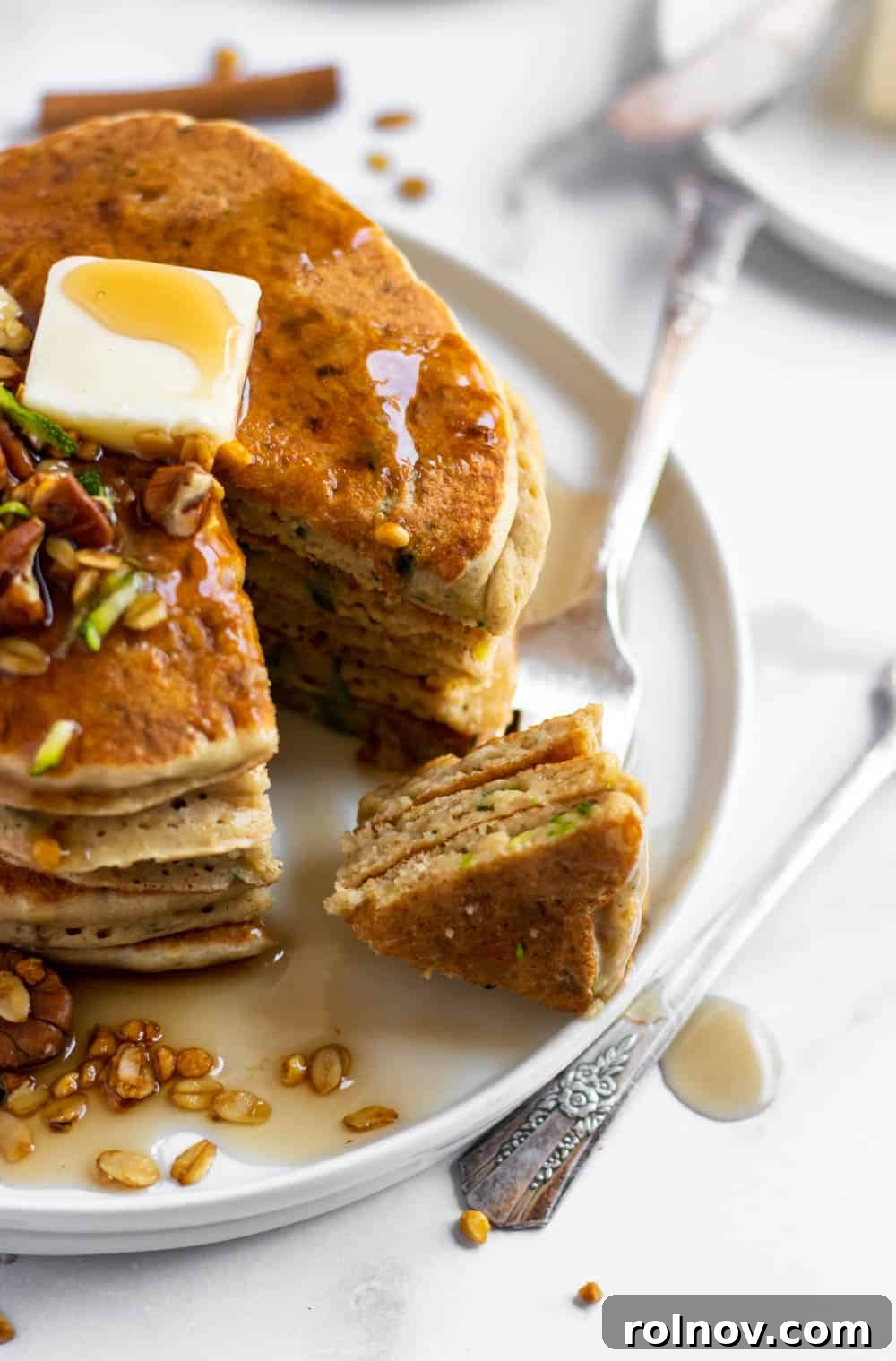 Wholesome Zucchini Oat Pancakes 4 Stack of zucchini oat flour pancakes topped with a pat of butter and chopped pecans.