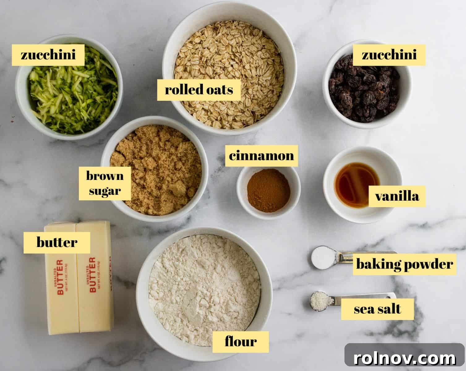 A flat lay photograph showcasing all the raw ingredients neatly arranged for making zucchini oatmeal bars, including oats, flour, brown sugar, butter, zucchini, and cinnamon.
