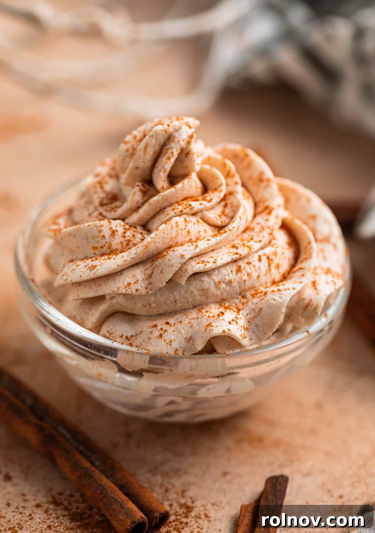 Autumn's Pumpkin Cloud 2 Pumpkin spice whipped cream piped into glass bowl with cinnamon dusted on top and cinnamon sticks beside it.