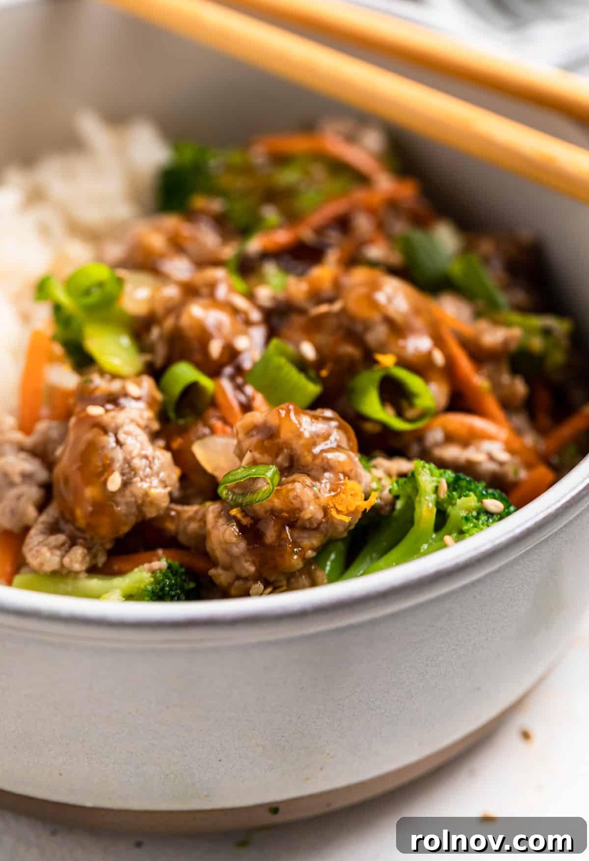 Sticky Teriyaki Pork Stir Fry 2 A beautifully plated bowl of Teriyaki Ground Pork Stir Fry, garnished with sesame seeds and green onions, with chopsticks resting on the side.