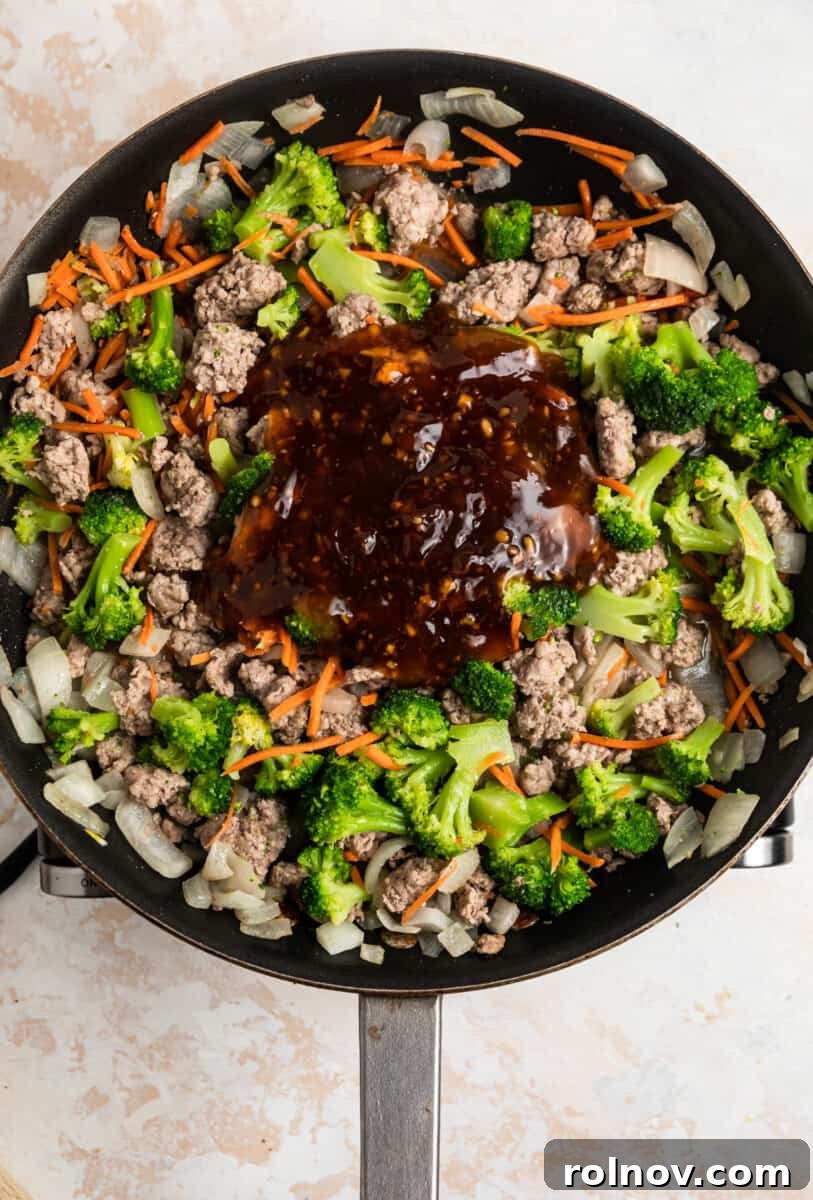 Sticky Teriyaki Pork Stir Fry 9 Homemade teriyaki sauce being poured over the ground pork and vegetable stir fry in a skillet.