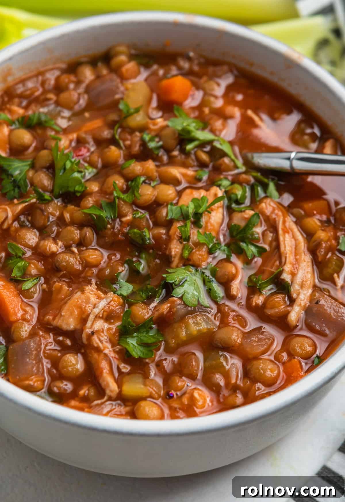 Turkey lentil soup in white bowl with spoon and chopped parsley on top.