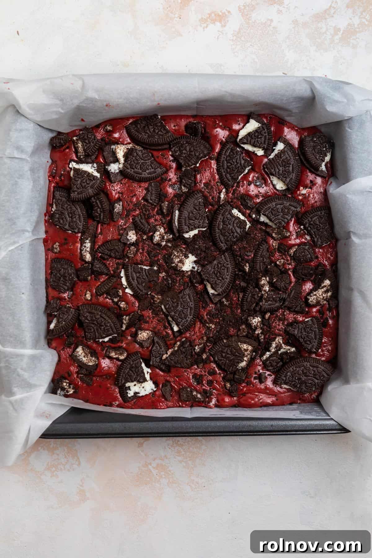 Prepared fudge in parchment lined baking pan and topped with crushed up Oreos.