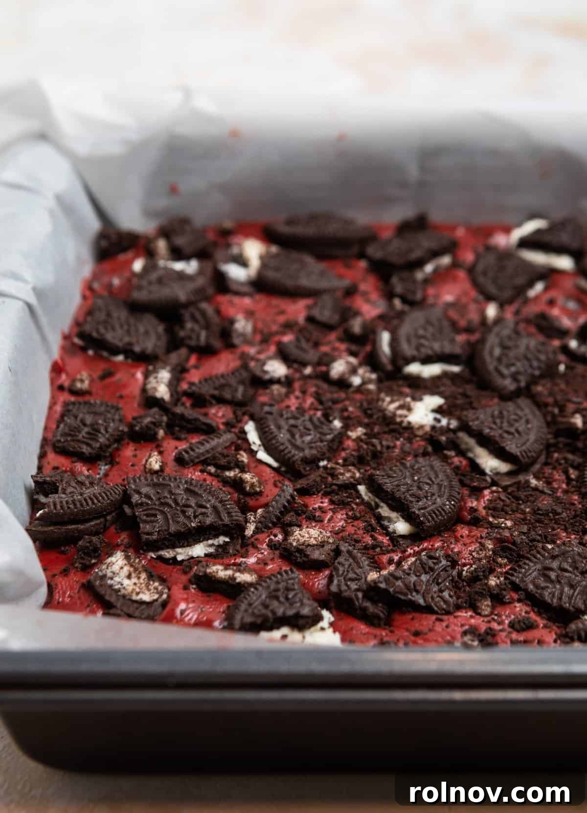 Oreo red velvet fudge in parchment lined pan and topped with crushed Oreos.