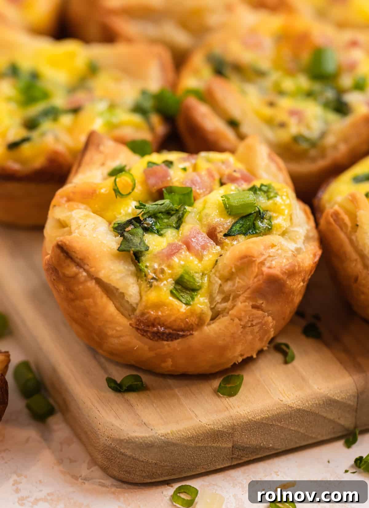 Buttery Flaky Quiche 2 Puff pastry mini quiches with ham and spinach on wood platter topped with green onion and parsley.