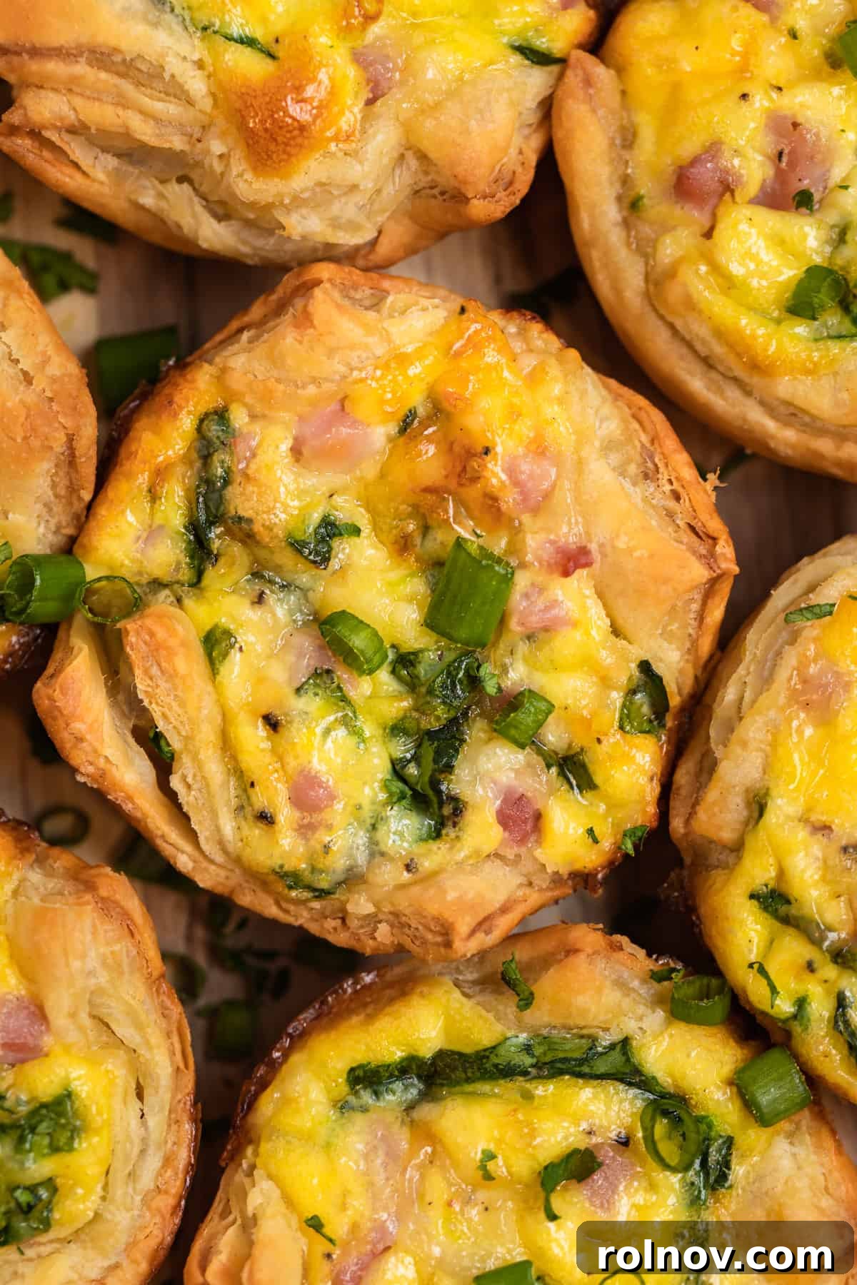 Buttery Flaky Quiche 13 Puff pastry mini ham and cheese quiche lined up on a wood board.