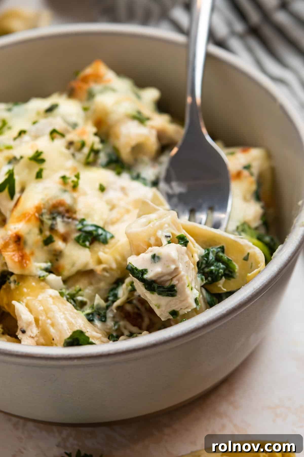 Spinach, chicken artichoke pasta casserole in bowl with fork.