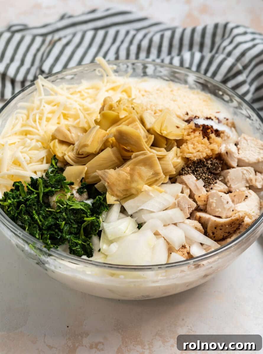 Spinach, artichokes, chicken, onion, cheese and other ingredients in mixing bowl.
