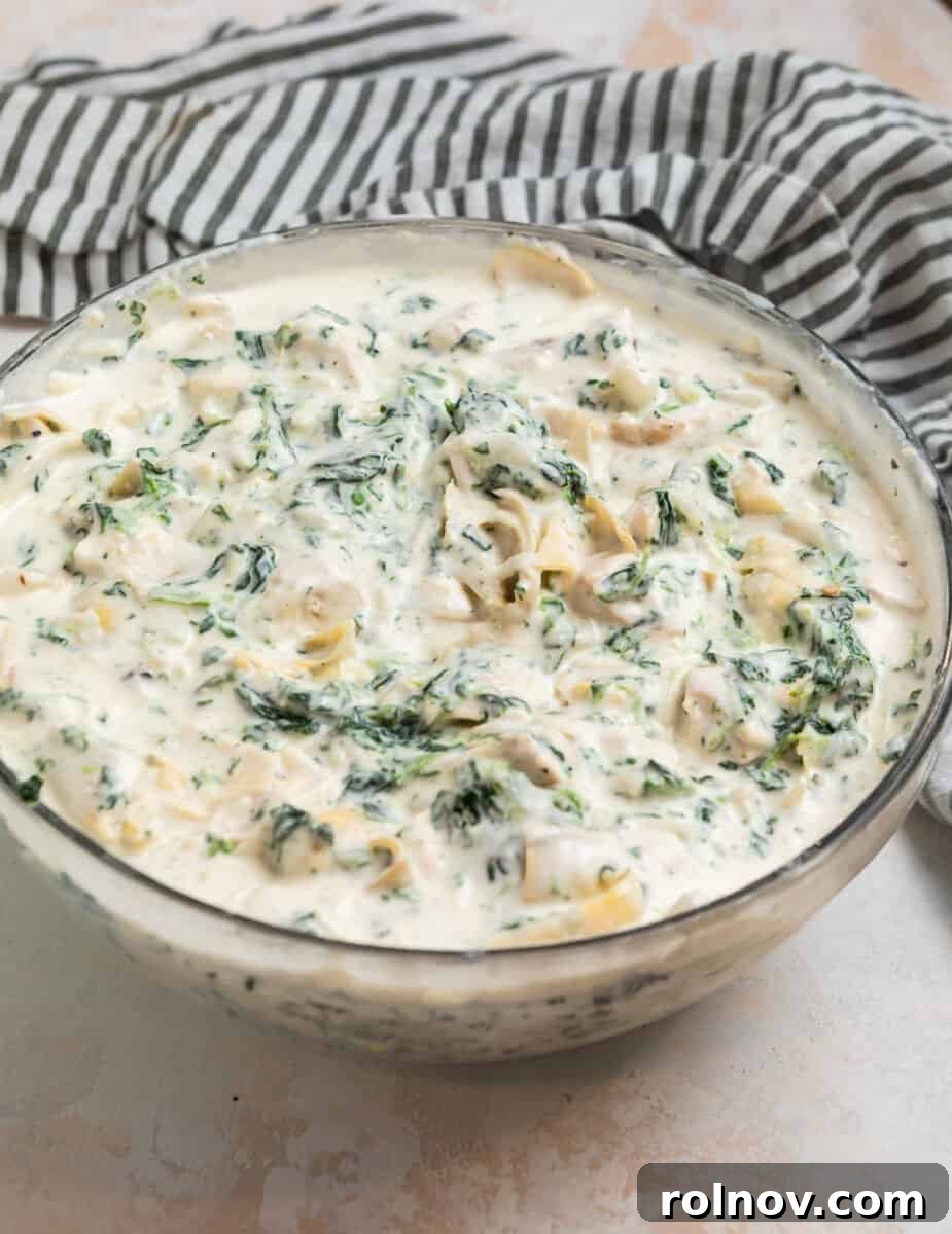 Spinach artichoke chicken creamy mixture in glass mixing bowl.