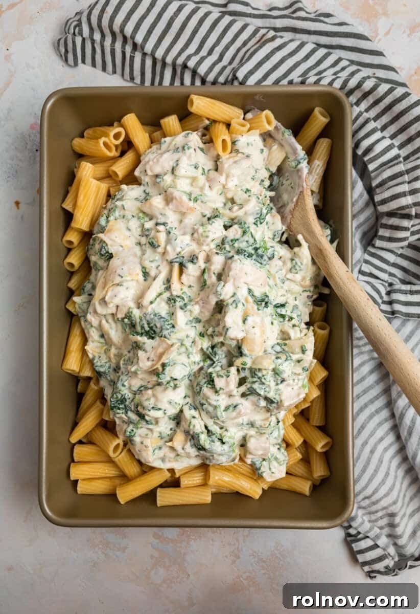 Spinach artichoke and chicken mixture over past in pan.