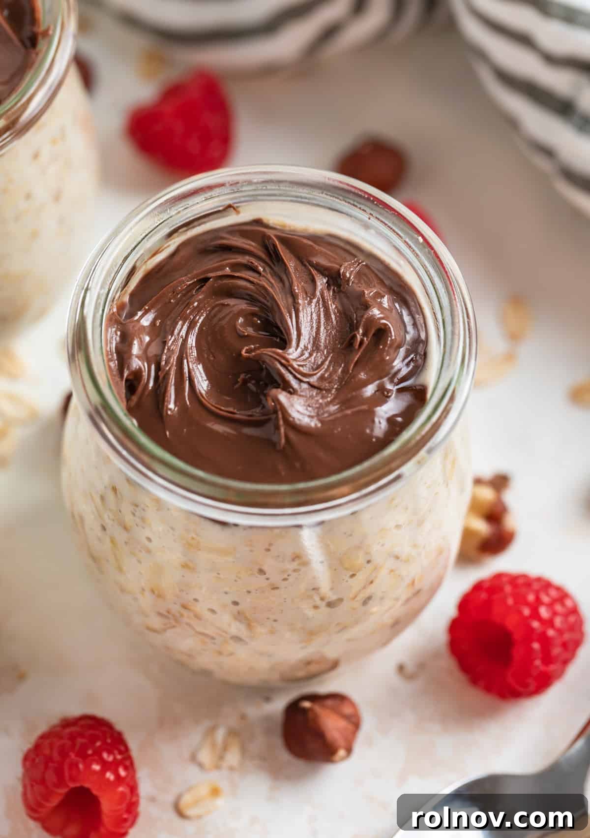 A jar of rich Nutella Overnight Oats, swirled with creamy hazelnut spread and topped with fresh raspberries and crunchy hazelnuts, ready for a delightful breakfast.