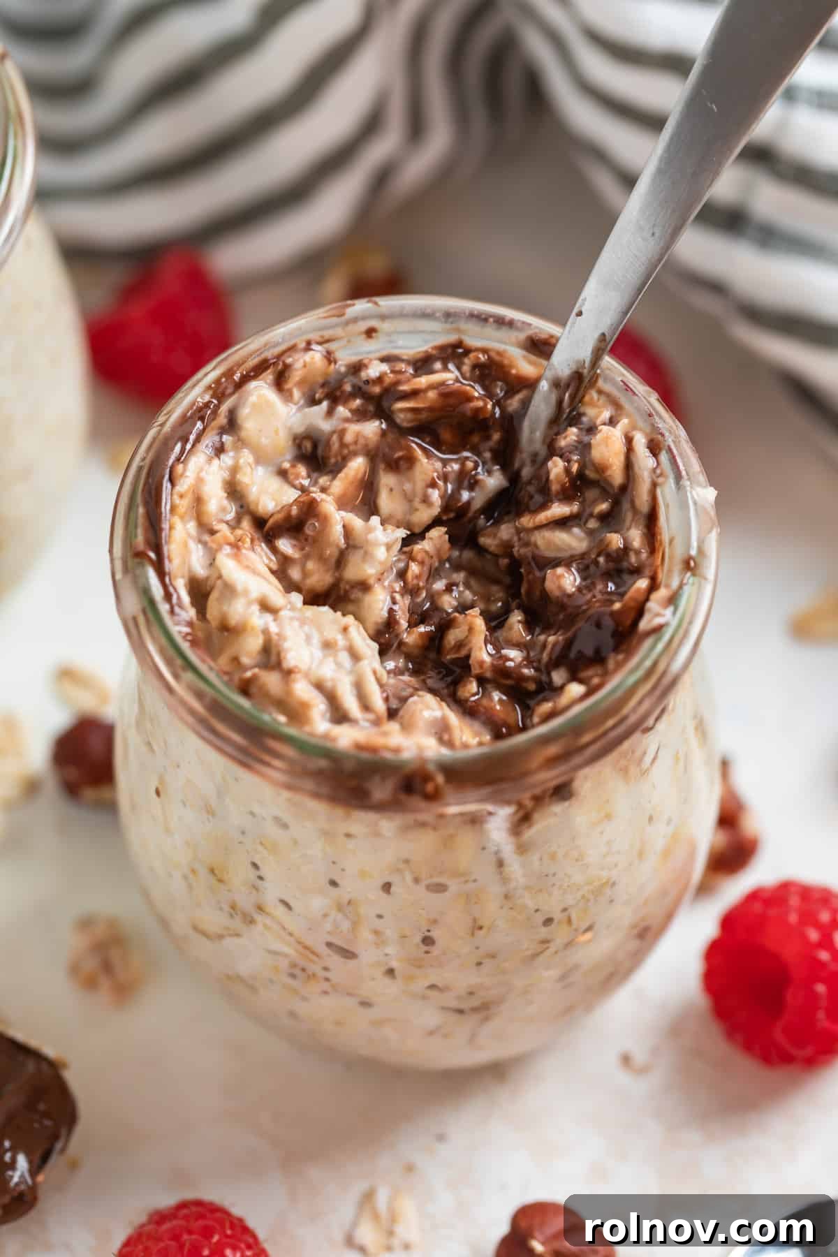 A jar of luscious Nutella Overnight Oats, with a spoon scooped in, showcasing its creamy texture and rich chocolate swirl, ready to be enjoyed.