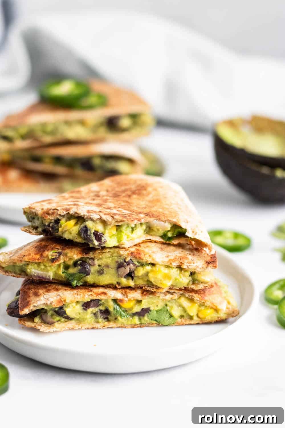 A close-up bite shot of a vegan black bean quesadilla with avocado on a white plate, highlighting the creamy filling and crispy tortilla.