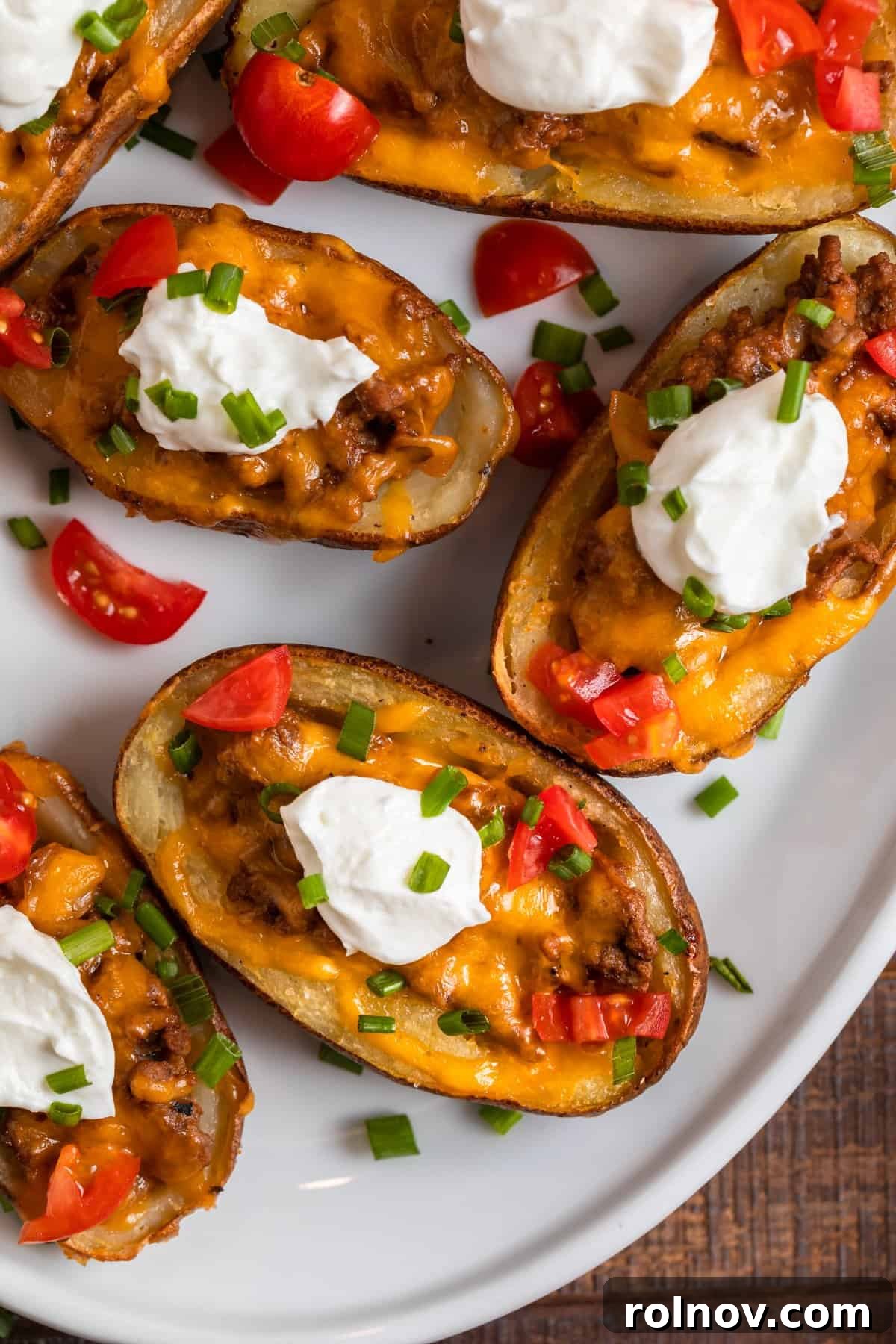 Cheesy Burger Potato Boats 14 Cheeseburger stuffed potato skins on white serving dish with chopped tomatoes, chives and sour cream.