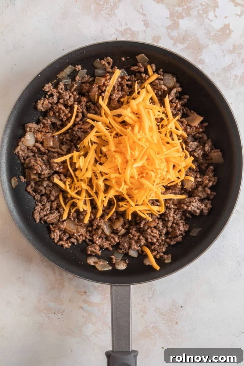 Cheesy Burger Potato Boats 9 Cheese topped ground beef in skillet.