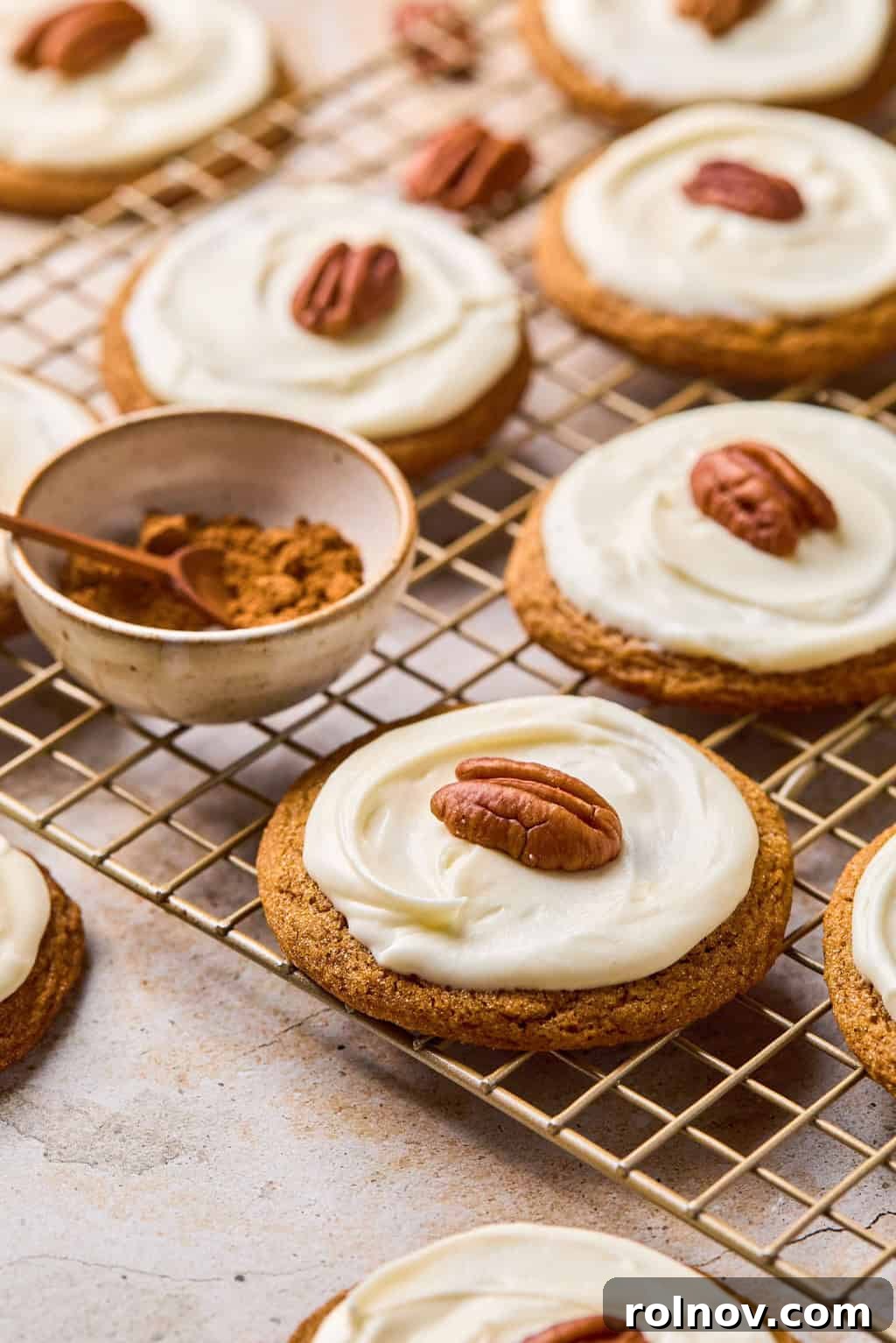 Golden Spiced Molasses Pumpkin Chews 2 Molasses cookies on cooling rack with icing and pecan on top.