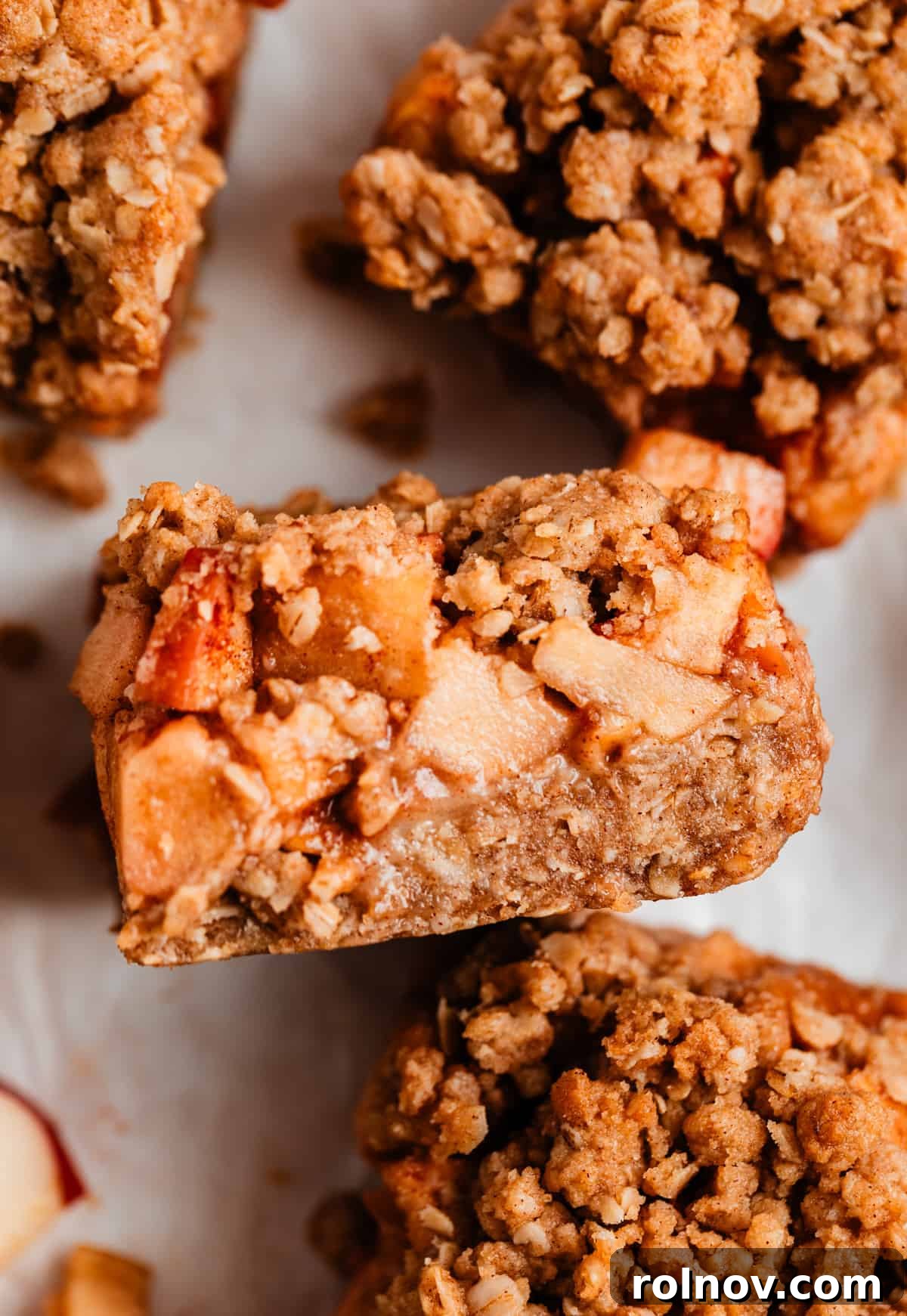 Golden Apple Crumble Bars 2 Golden-brown apple crumble bars cooling on parchment paper, revealing delicious layers of oat crust, apple filling, and crumbly topping.