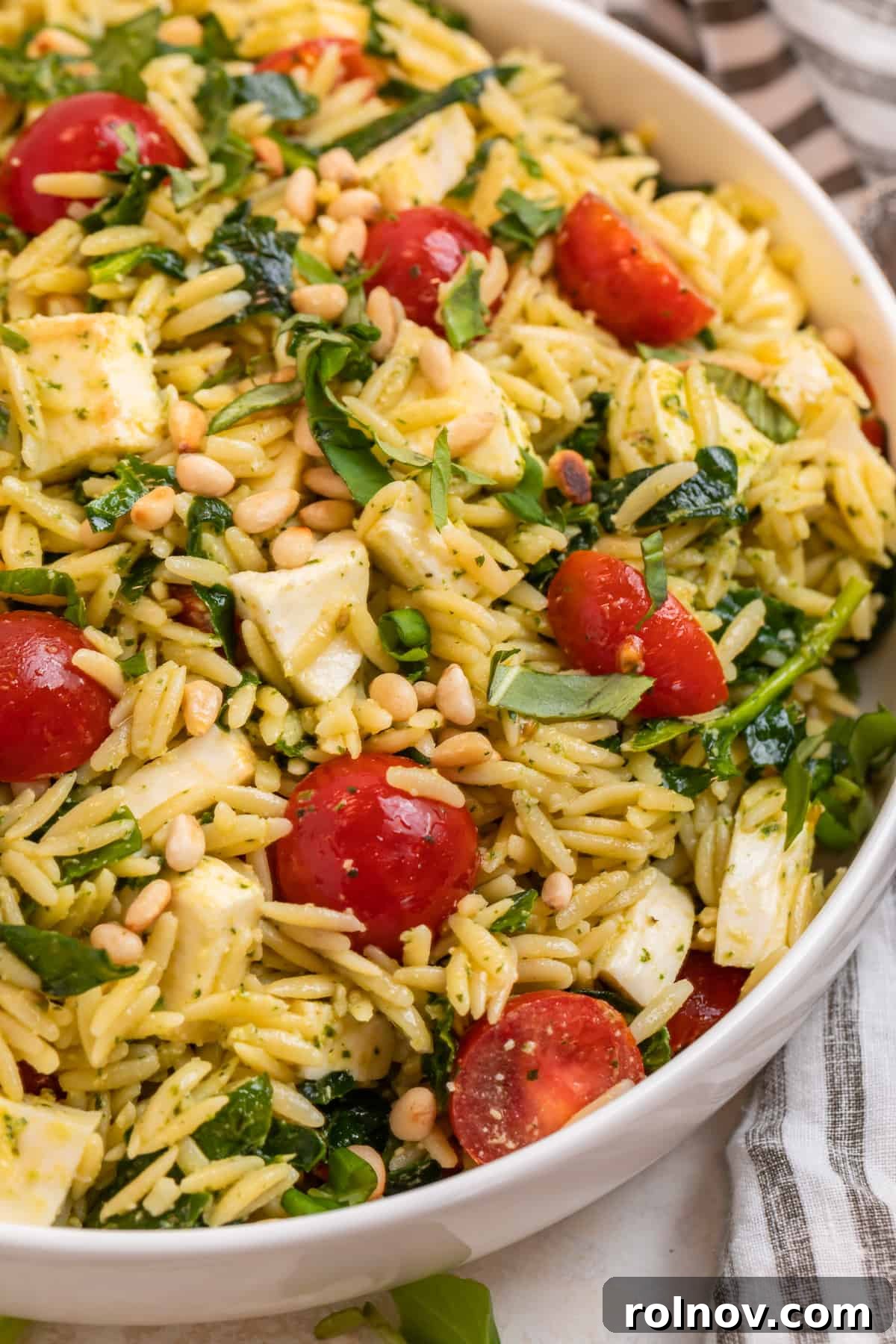 Emerald Orzo Pesto Salad 2 Pesto orzo salad with cherry tomatoes, mozzarella and spinach in white bowl.