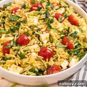 Pesto orzo salad in white bowl topped with freshly chopped basil and toasted pine nuts.