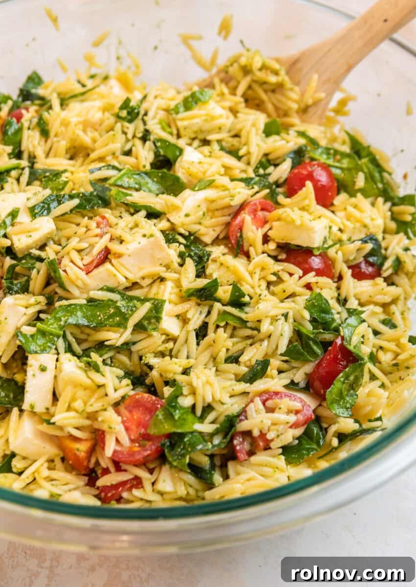 Emerald Orzo Pesto Salad 9 Pesto orzo salad in mixing bowl with wood spoon.