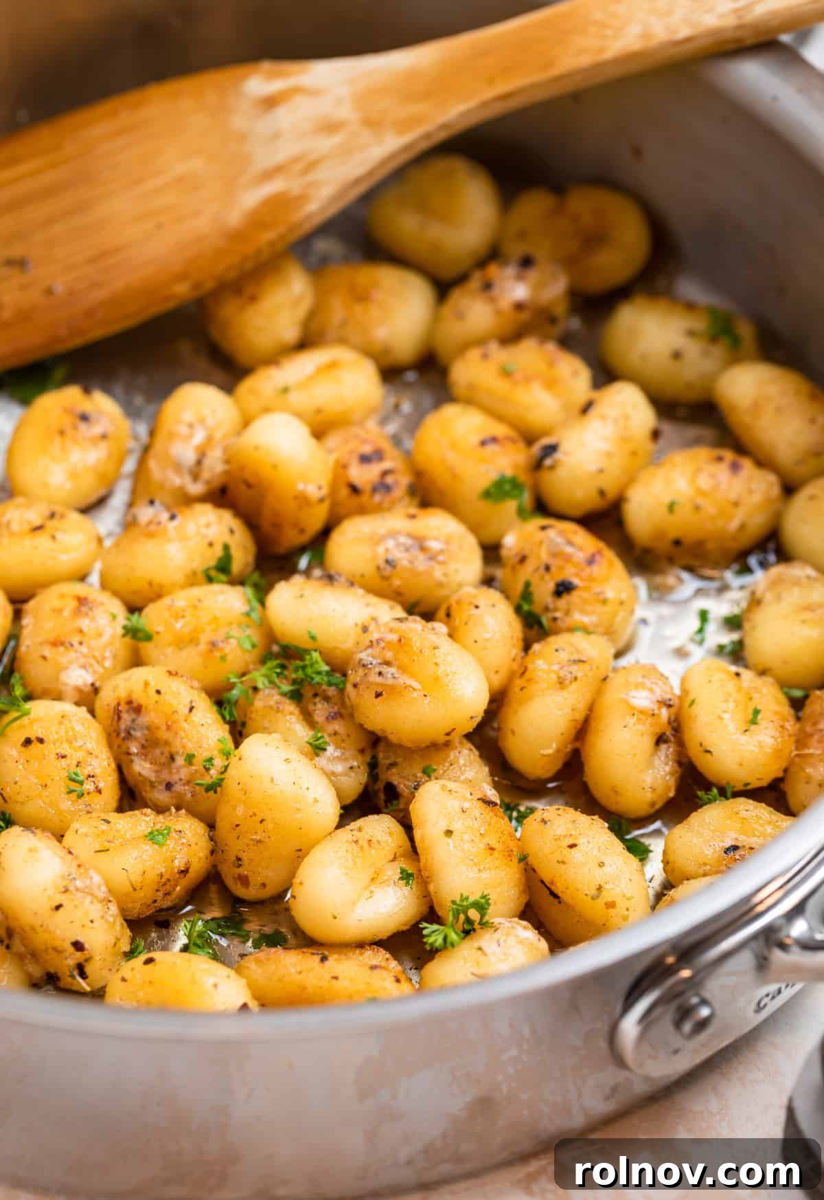 Golden Skillet Gnocchi 2 Golden brown pan-fried gnocchi sizzling in a skillet, garnished with fresh chopped parsley and a wooden spoon resting nearby.