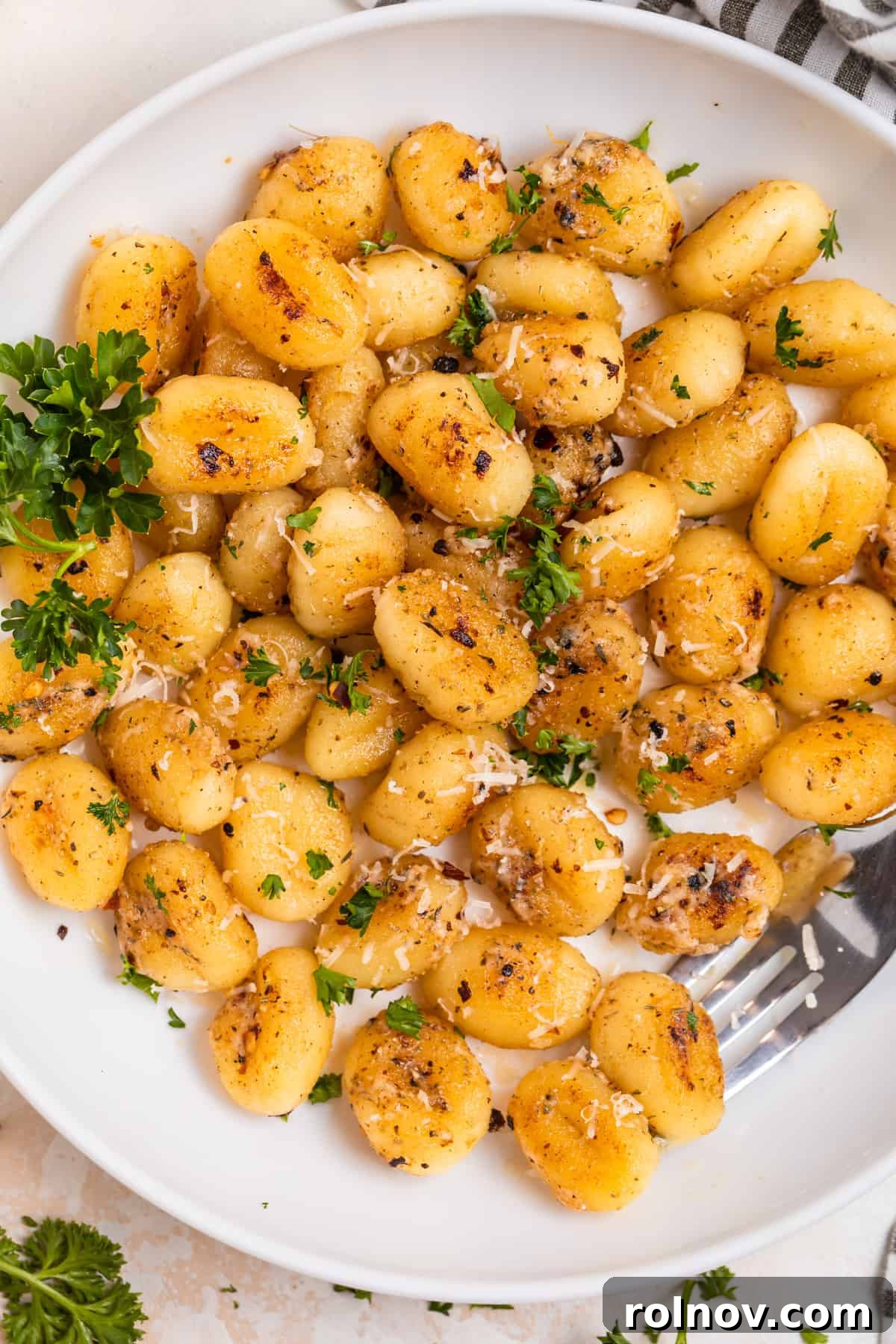 Golden Skillet Gnocchi 11 Overhead shot of a white plate with golden pan-fried gnocchi, garnished with fresh Parmesan cheese and vibrant chopped parsley.
